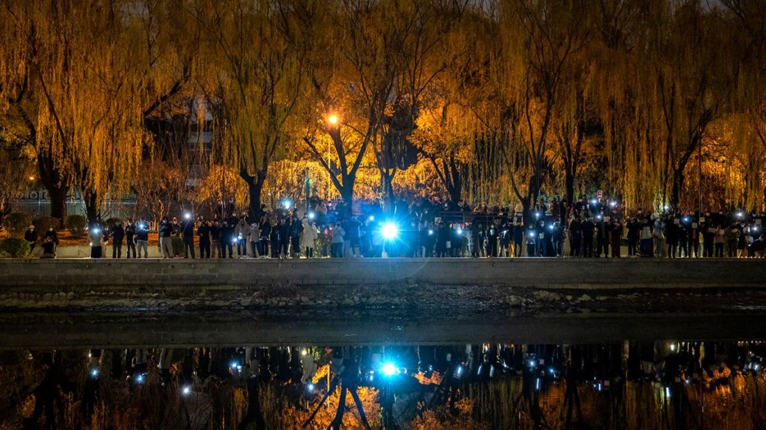 Los manifestantes sostienen sus teléfonos móviles durante una protesta contra las estrictas medidas de cero covid de China en el río Liangma el 27 de noviembre de 2022 en Beijing, China.