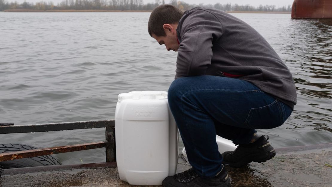 Un hombre llena contenedores con agua del río Dnipro, con el territorio controlado por Rusia justo al otro lado de la vía fluvial.