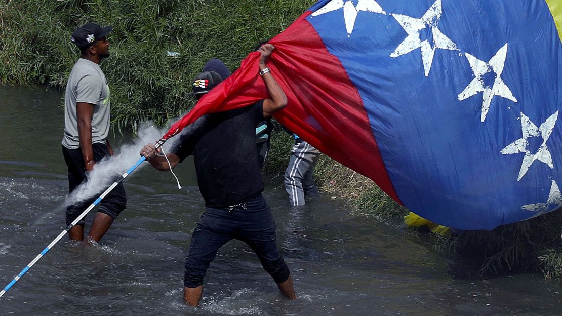 Un migrante venezolano sostiene una bandera mientras cruza el río Bravo (también río Grande) de regreso a Ciudad Juárez, México, después de una manifestación contra las políticas de inmigración de Estados Unidos junto a la valla fronteriza, el 31 de octubre de 2022. Crédito: HERIKA MARTINEZ/AFP a través de Getty Images.