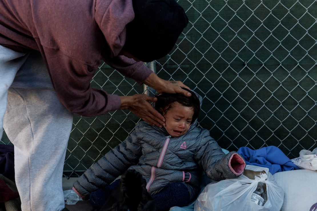 Carlos Pavón Flores, a la izquierda, frota loción en el rostro de su hija Esther para protegerla del viento y el frío mientras acampan frente a la estación de autobuses Greyhound en El Paso.