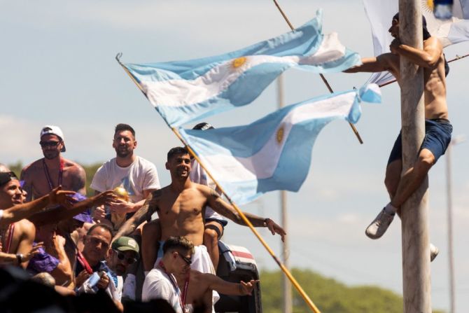 Un hincha colgado de un poste celebra mientras pasa el autobús con Messi y los jugadores.