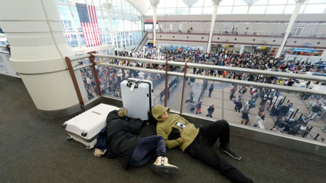 Un par de viajeros duermen mientras otros hacen fila para pasar por un control de seguridad en el Aeropuerto Internacional de Denver el viernes.