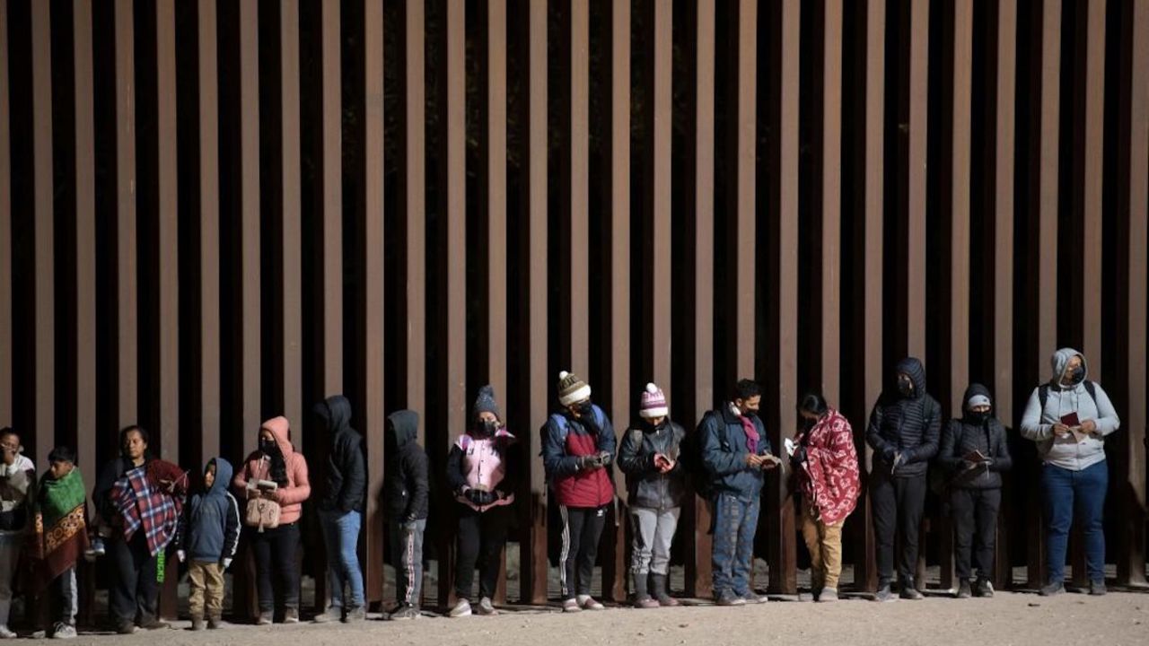 TOPSHOT - Asylum-seekers line up to be processed by US Customs and Border Patrol agents at a gap in the US-Mexico border fence near Somerton, Arizona, on December 26, 2022. - The United States is seeing a rising number of asylum-seekers turning themselves in at the US-Mexico border in anticipation of the lifting of Title 42, a pandemic-era policy used to bar migrants from entering the US. (Photo by Rebecca NOBLE / AFP)