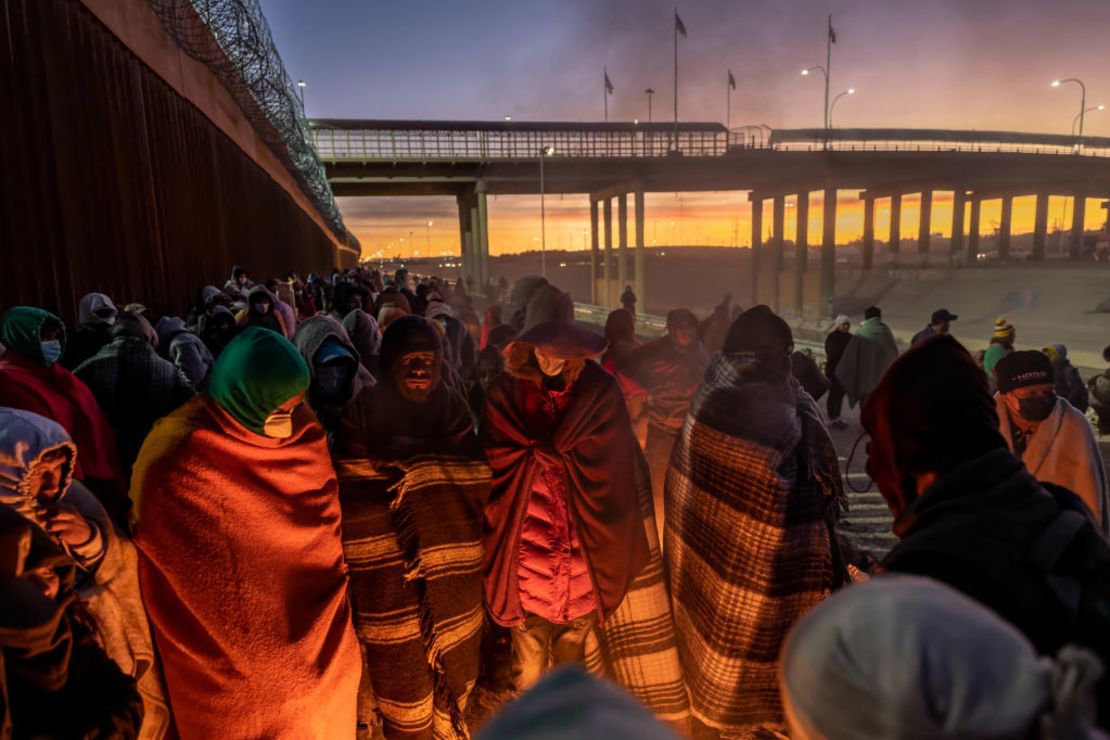 Los inmigrantes se calientan junto a una fogata al amanecer después de pasar una noche junto a la valla fronteriza entre Estados Unidos y México el 22 de diciembre de 2022 en El Paso, Texas.