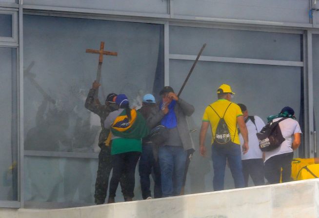 Se ve a simpatizantes de Bolsonaro cargando una cruz al romper una ventana del Palacio Presidencial de Planalto en Brasilia.