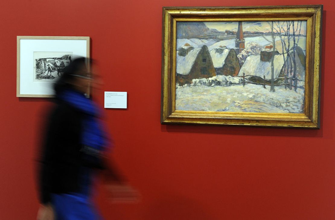 Esta fotografía tomada en marzo de 2016 muestra a una persona caminando delante de la obra de 1894 del artista Paul Gauguin titulada "Pueblo bretón bajo la nieve".