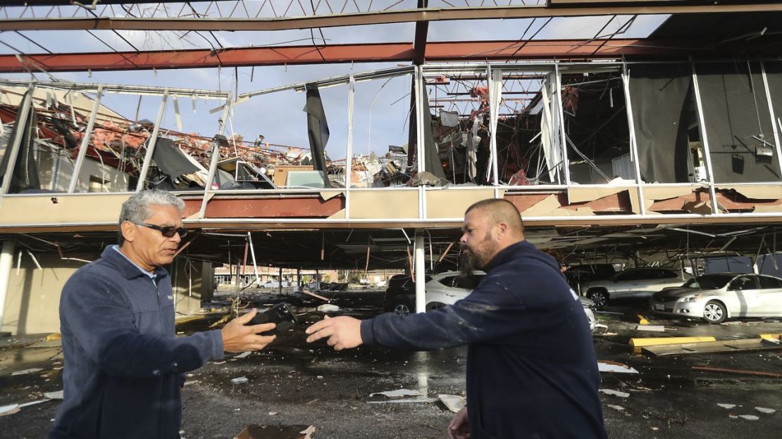 Los empleados de Mr. Electric, Héctor Vázquéz, a la izquierda, y Lucas Perry se pasan un teléfono afuera del edificio de su oficina donde estaban trabajando cuando una poderosa tormenta azotó el martes en Deer Park, Texas.