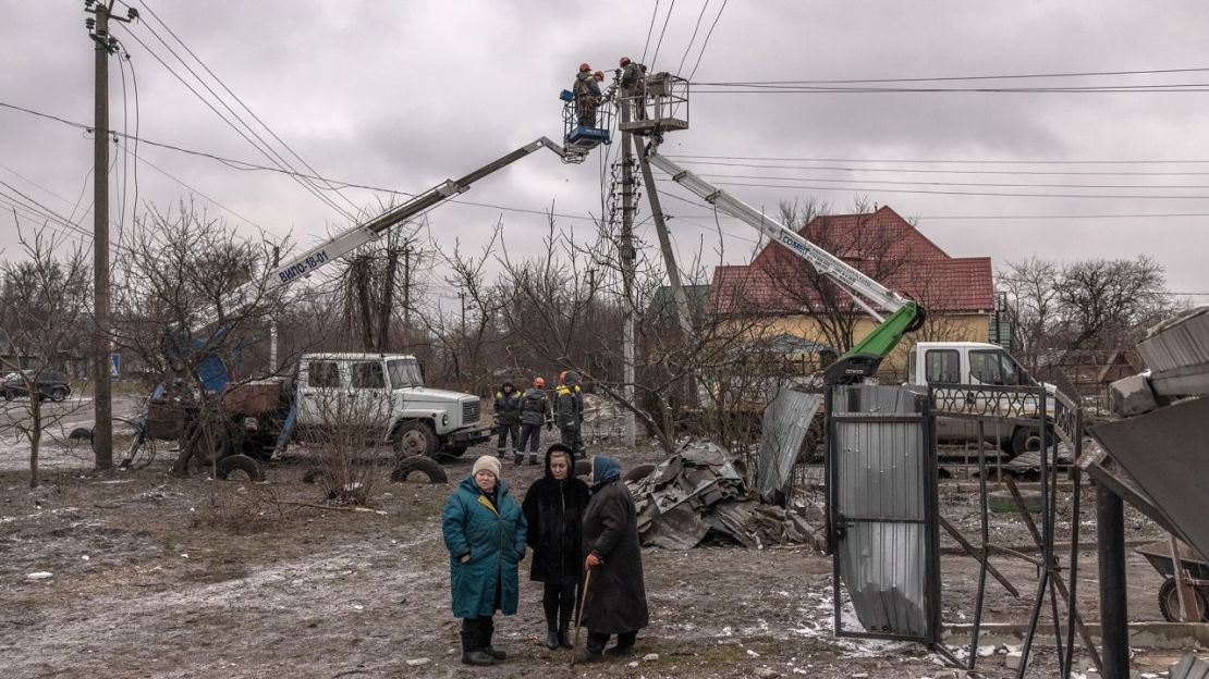 Las mujeres se paran junto a las casas dañadas, mientras los trabajadores intentan reparar los cables eléctricos luego de los ataques con misiles rusos el 26 de enero de 2023 en Hlevakha, en las afueras de Kyiv, Ucrania. Crédito: Roman Pilipey/Getty Images