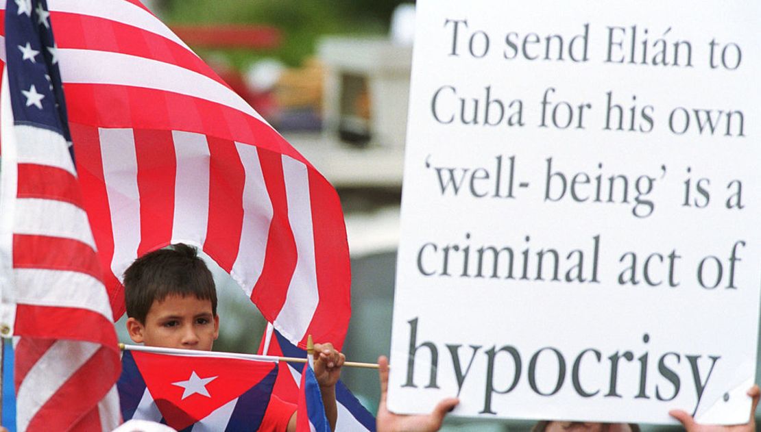 Un simpatizante de la familia de Elián González en Miami se sienta junto a un cartel frente a la casa donde vivía Elián en Miami el 15 de abril de 2000. El cartel dice: "Enviar a Elián a Cuba por su propio 'bienestar' es un acto criminal de hipocresía".