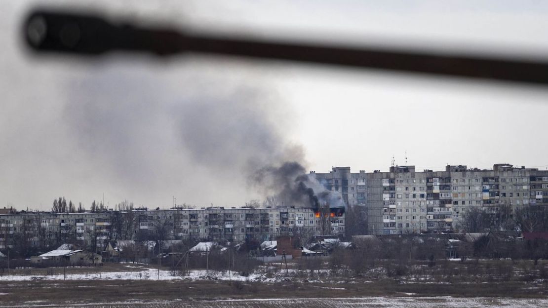 Un vehículo militar ucraniano pasa mientras un edificio de apartamentos alcanzado por la artillería rusa arde en la distancia el 14 de febrero de 2023 en Bakhmut, Ucrania.