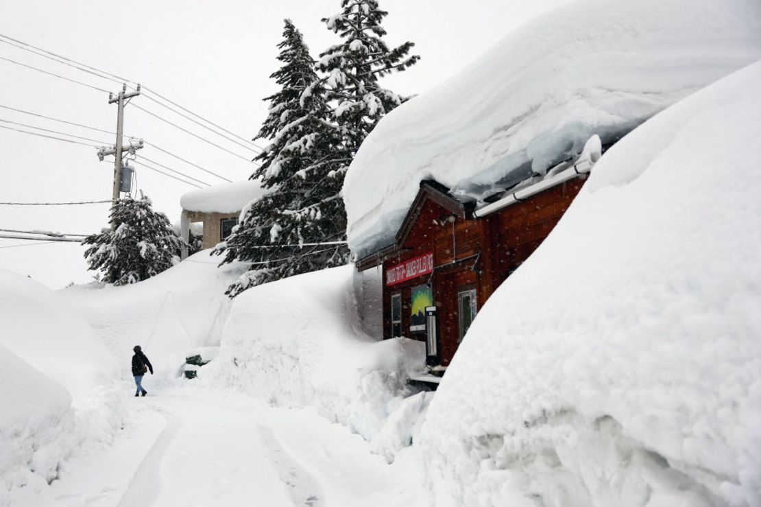 Una persona pasa junto a un restaurante mientras la nieve cae sobre los bancos de nieve acumulados de tormentas anteriores durante otra tormenta de invierno en las montañas de Sierra Nevada el 10 de marzo de 2023 en Mammoth Lakes, California.