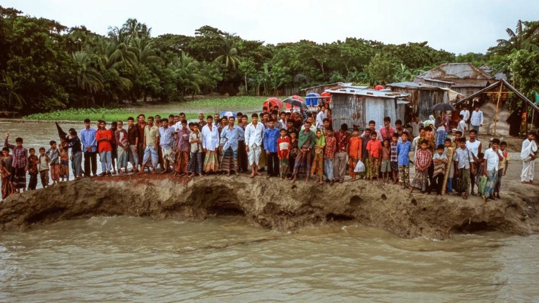 Aldeanos en los restos de una carretera en la isla de Bhola, Bangladesh, en 2005. La zona, en la desembocadura del delta del Ganges, sigue sufriendo una erosión acelerada debido a la subida del nivel del mar. Crédito: © Gary Braasch/naturepl.com