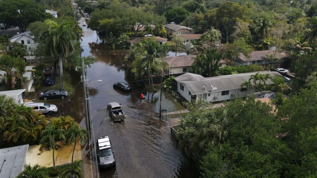 Camiones y un residente a pie se abren paso a través del retroceso de las aguas de la inundación en el barrio Sailboat Bend de Fort Lauderdale, Florida, el jueves 13 de abril de 2023.