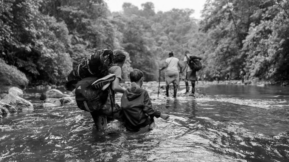 Una mujer venezolana guía a su hijo a través del agua hasta la rodilla, con su dinosaurio de juguete metido de forma segura en su sudadera. Ella espera llevarlos a Estados Unidos para reunirse con su esposo.