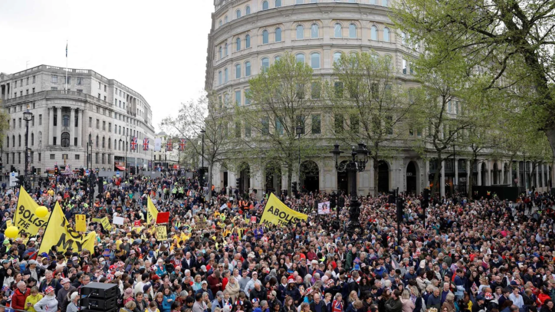 Manifestantes sostienen pancartas en las que se lee "No es mi Rey" y "Abolir la Monarquía" cerca de la procesión.