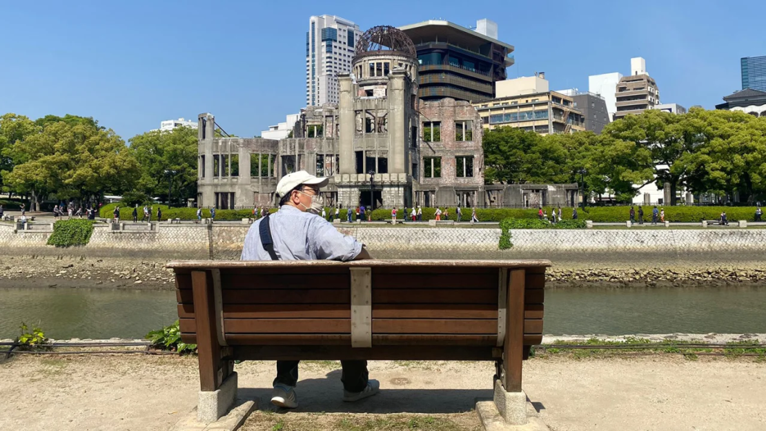 Un hombre se relaja junto al río en un banco con vista a la cúpula Genbaku.