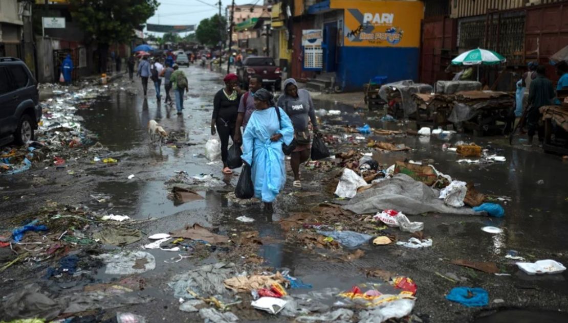 Varias personas se abren paso entre charcos mientras caminan en medio de una calle llena de basura tras las fuertes lluvias caídas en Puerto Príncipe.Ariana Cubillos/AP