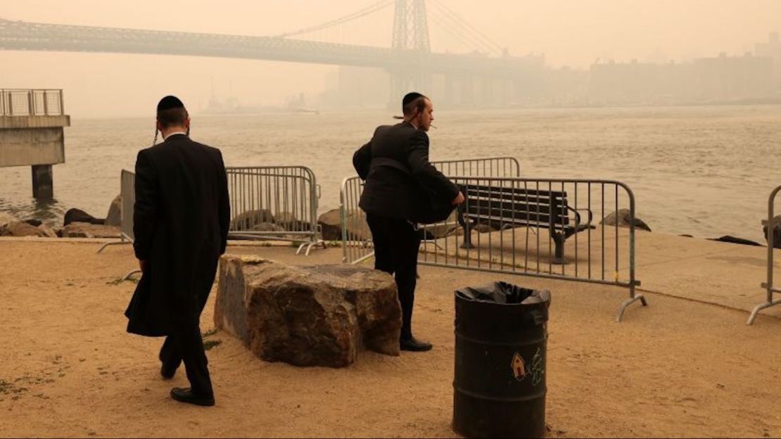 Dos hombres judíos ortodoxos junto al mar mientras la neblina y el humo causados por los incendios forestales en Canadá cubren el horizonte de Manhattan, en Brooklyn, Nueva York, el miércoles.