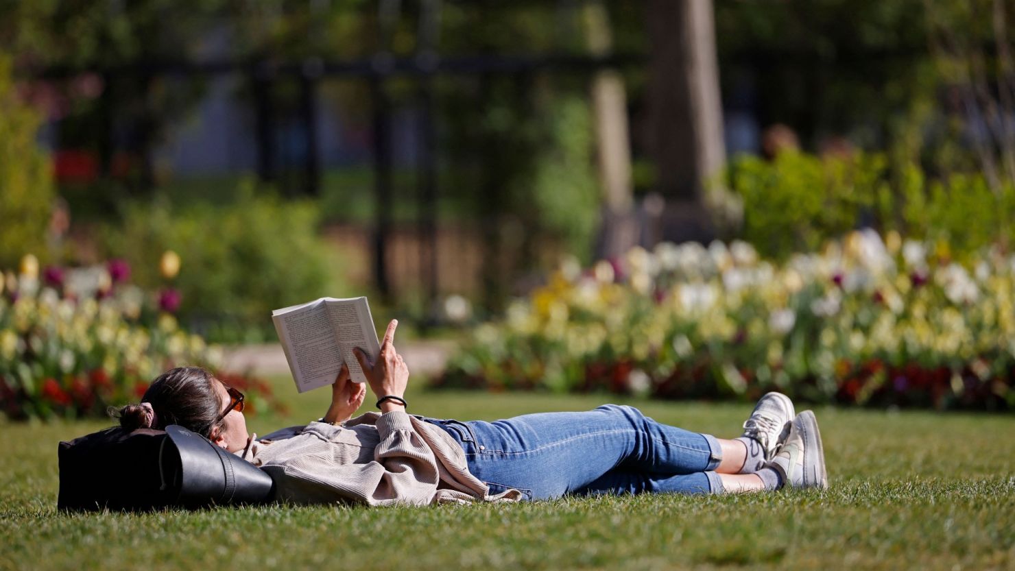 Una mujer lee un libro en el césped de Hyde Park bajo el sol de Londres.