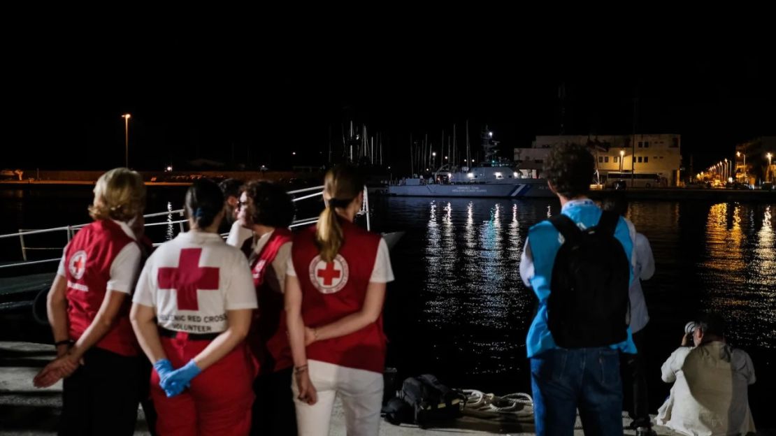 Miembros de la Cruz Roja y la ACNUR ante un hangar de migrantes mientras un barco de la guardia costera con 79 cadáveres llega al puerto griego de Kalamata. Crédito: Byron Smith/Getty Images