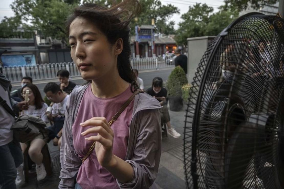 Una mujer se refresca con un ventilador mientras espera una mesa afuera de un popular restaurante local durante una ola de calor el 23 de junio de 2023 en Beijing, China.