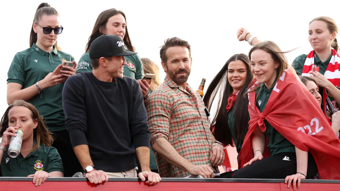 McElhenney y Reynolds celebran con las jugadoras del equipo femenino del Wrexham durante un desfile en autobús tras la temporada ganadora del título.