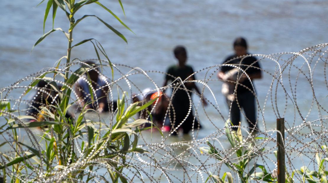 Migrantes caminan detrás de una alambrada en el agua a lo largo de la frontera del río Grande con México en Eagle Pass, Texas, el 15 de julio de 2023.