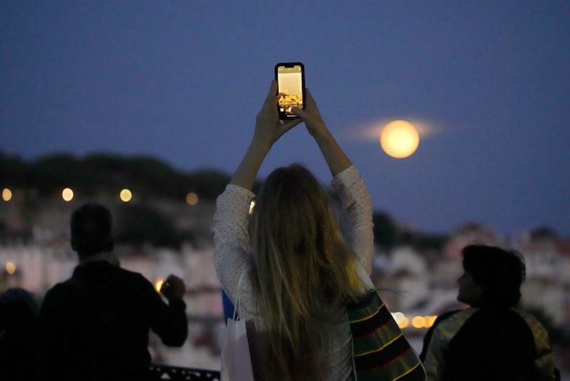 Una mujer toma fotos de la luna azul que se eleva sobre Lisboa, Portugal, el 30 de agosto.