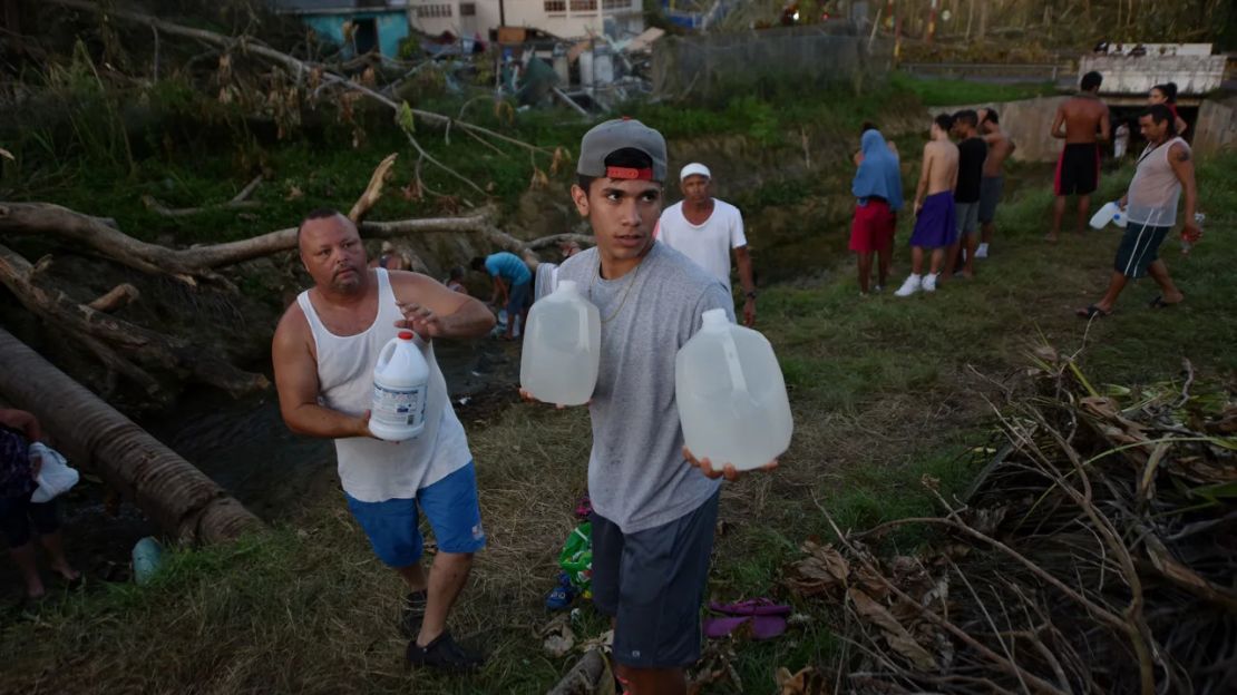 Personas cargan agua en botellas recuperadas de un canal debido a la falta de agua tras el paso del huracán María en Puerto Rico en septiembre de 2017.