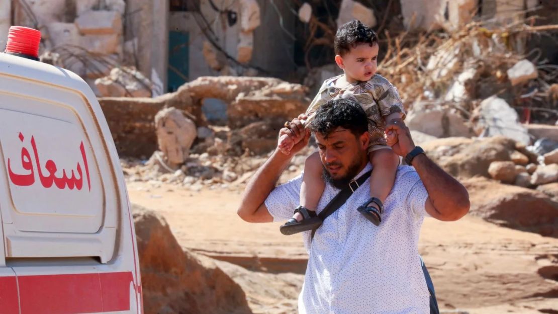 Un hombre lleva a un niño al hombro mientras pasa por una zona dañada por las inundaciones repentinas en Derna el 14 de septiembre. Crédito: Abdullah Doma/AFP/Getty Images