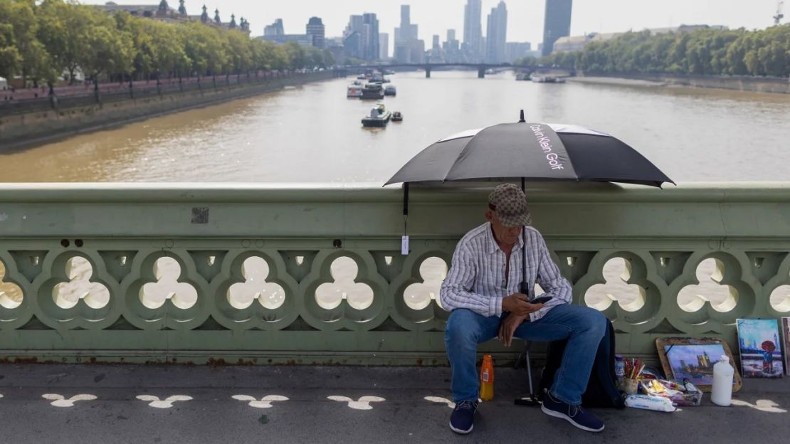 Un artista se sienta bajo la sombra de una sombrilla en el puente de Westminster durante un clima cálido en Londres el 6 de septiembre.