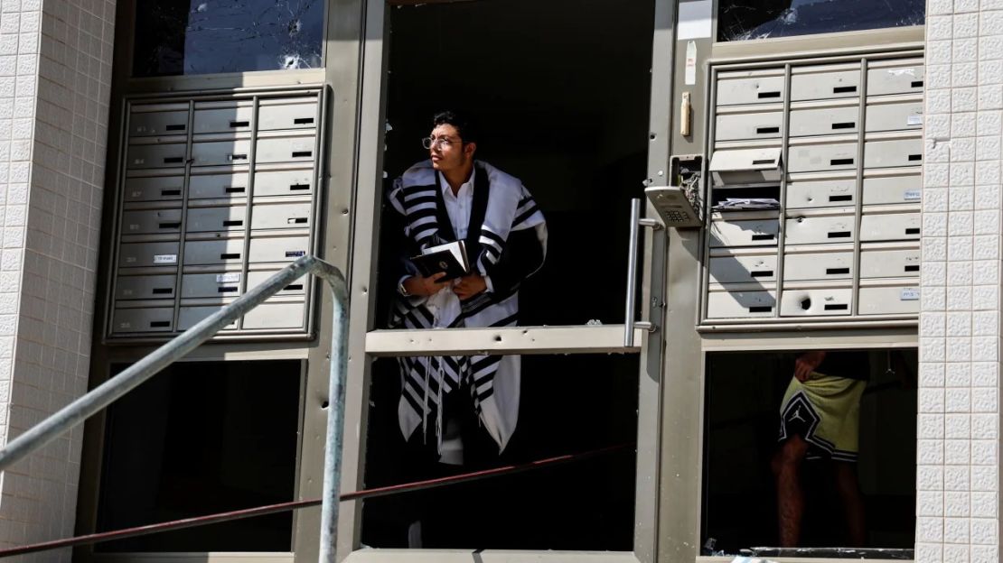 Un hombre que lleva un chal de oración judío mira desde la entrada dañada de un edificio, mientras se lanzan cohetes desde Gaza, en Ashkelon, al sur de Israel.