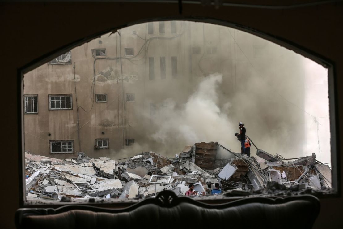 Palestinos inspeccionan un edificio destruido mientras los equipos de emergencia tratan de contener el fuego tras el bombardeo de Gaza por aviones israelíes el 7 de octubre.