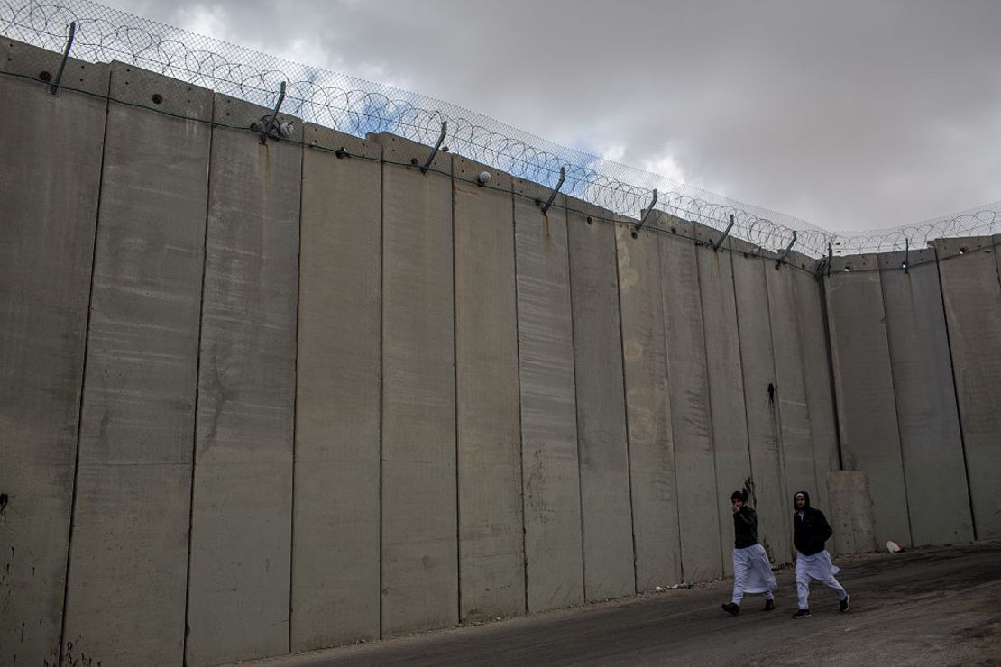 Dos hombres caminan junto a un muro del lado israelí del barrio dividido Abu Dis, en Jerusalén