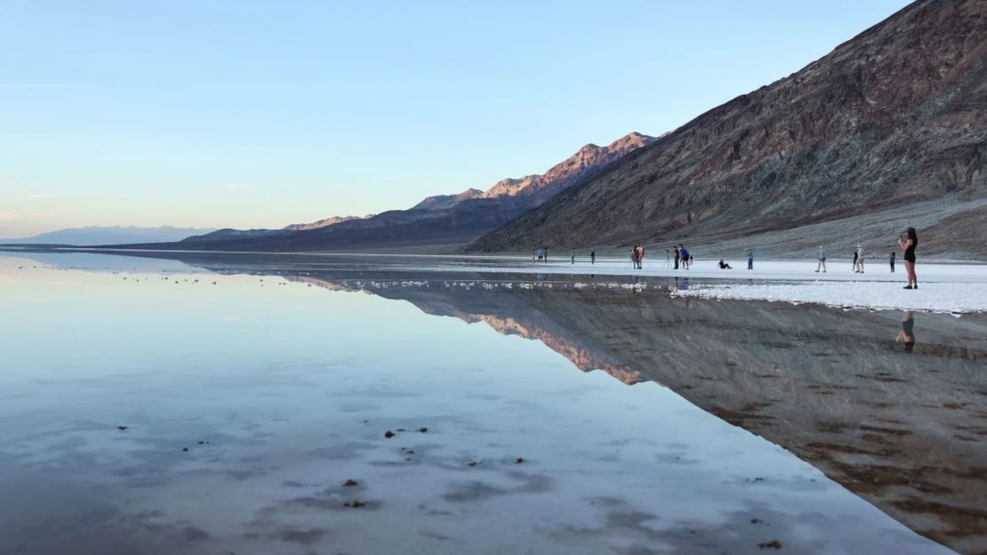 Los visitantes se reúnen en el extenso lago temporal en las salinas de la cuenca de Badwater en el recientemente reabierto Parque Nacional del Valle de la Muerte el 21 de octubre de 2023.