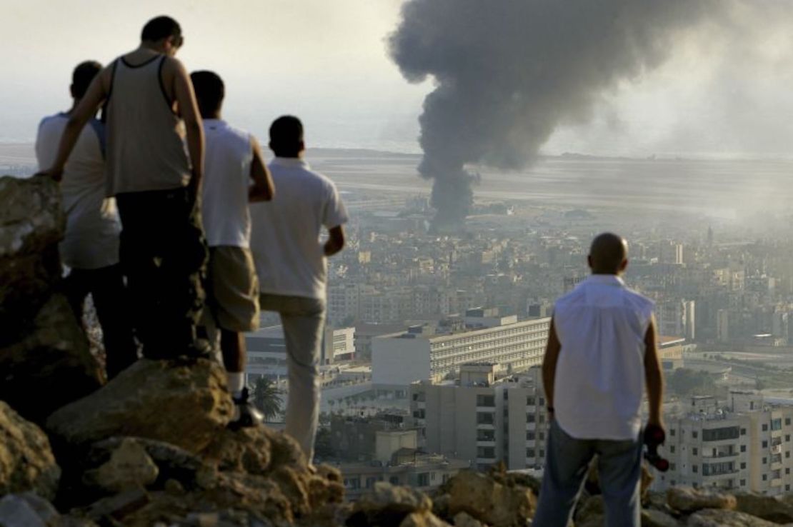 Jóvenes libaneses se reúnen en la cima de una colina que domina la ciudad de Beirut para observar el humo que sigue saliendo de un vertedero de combustible en el aeropuerto internacional de Beirut, que fue alcanzado por un ataque aéreo israelí, en 2006.