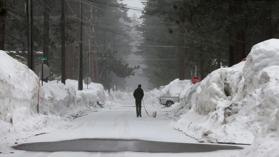 Un hombre pasea a su perro por una calle cubierta de nieve mientras la nieve comienza a caer durante un río atmosférico el 21 de marzo de 2023 en South Lake Tahoe, California.