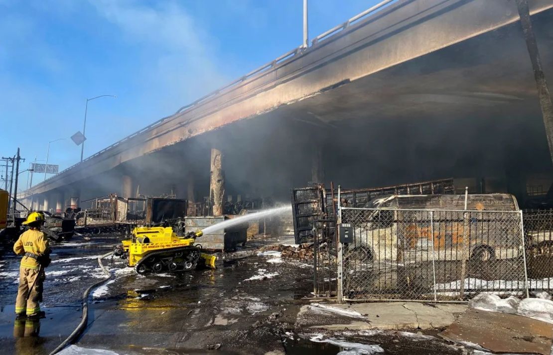 Un bombero de Los Ángeles utiliza una manguera robótica para apagar un incendio bajo la Interestatal 10 que dañó gravemente un paso elevado en el centro de Los Ángeles el sábado. Crédito: Caltrans Distrito 7/AP