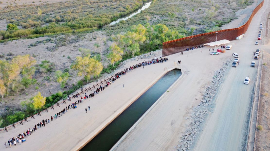 En una vista aérea, migrantes que buscan asilo en Estados Unidos esperan en fila cerca de la valla fronteriza para ser procesados por agentes de la Patrulla Fronteriza de Estados Unidos después de cruzar a Arizona desde México el 11 de mayo de 2023 en Yuma, Arizona.