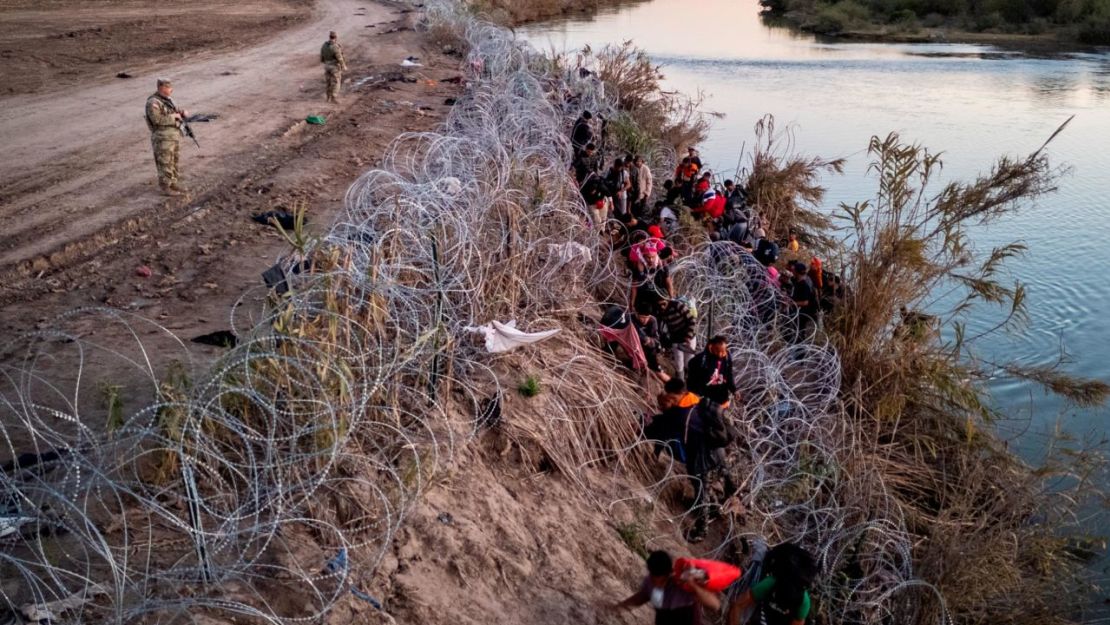 Agentes de la Guardia Nacional de Texas observan cómo los migrantes se abren paso a través de alambre de púas después de cruzar el Río Grande hacia Estados Unidos el 17 de diciembre en Eagle Pass, Texas. Crédito: John Moore/Getty Images