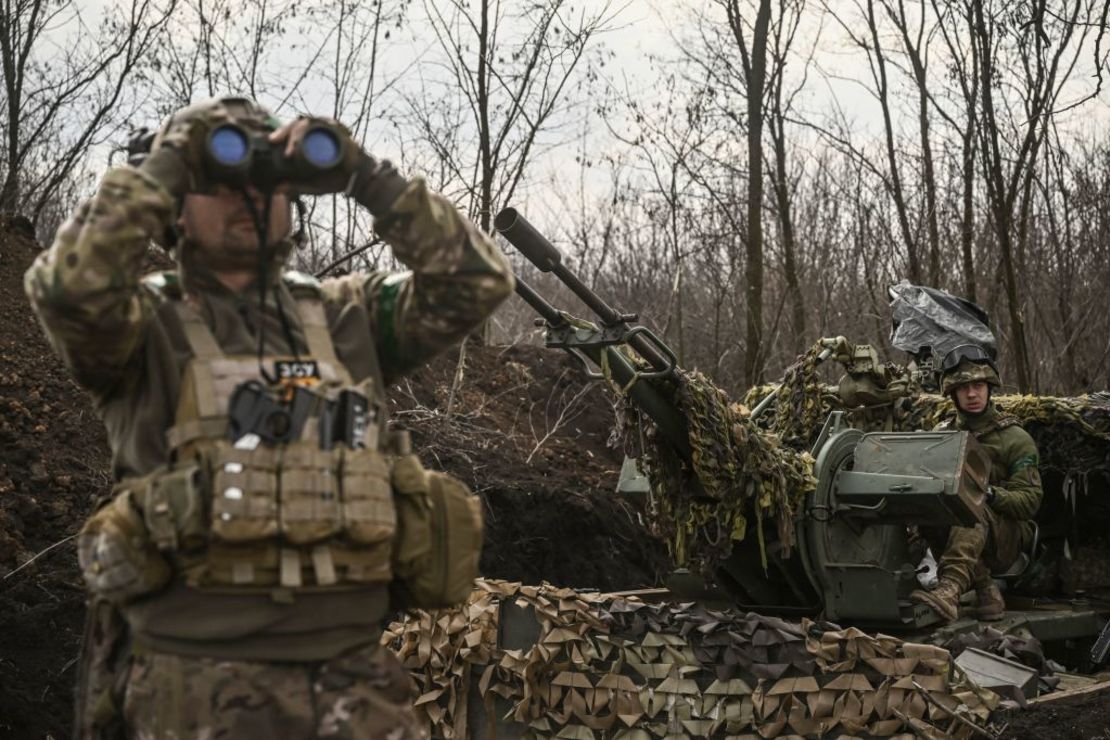 Un militar ucraniano (I) mira con gafas junto a otro (D) sentado en un cañón antiaéreo cerca de Bajmut, el 24 de marzo de 2023.