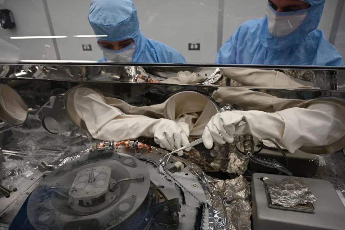 Los procesadores de astromateriales Mari Montoya (izquierda) y Curtis Calva utilizan herramientas para recoger partículas de asteroides de la base del recipiente científico de OSIRIS-REx. Crédito: NASA