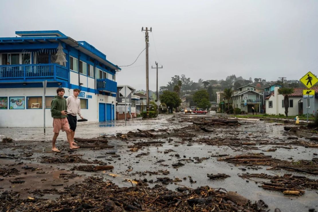 Dos hombres caminan entre escombros marinos en el barrio Río del Mar de Aptos, en el condado de Santa Cruz.