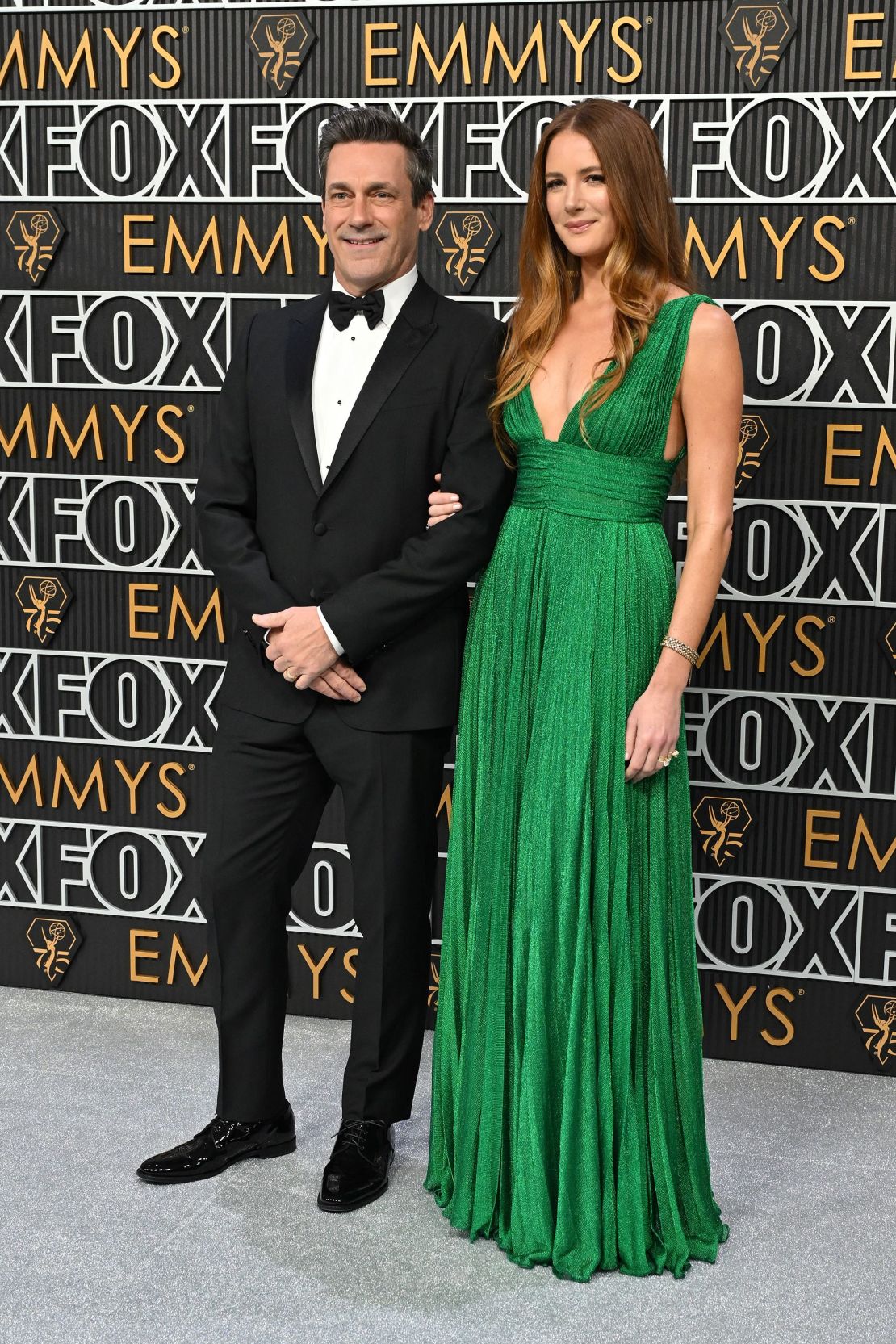 El esmoquin clásico de Jon Hamm y el brillante vestido plisado verde de su esposa Anna Osceola eran ambos de Dolce & Gabbana.