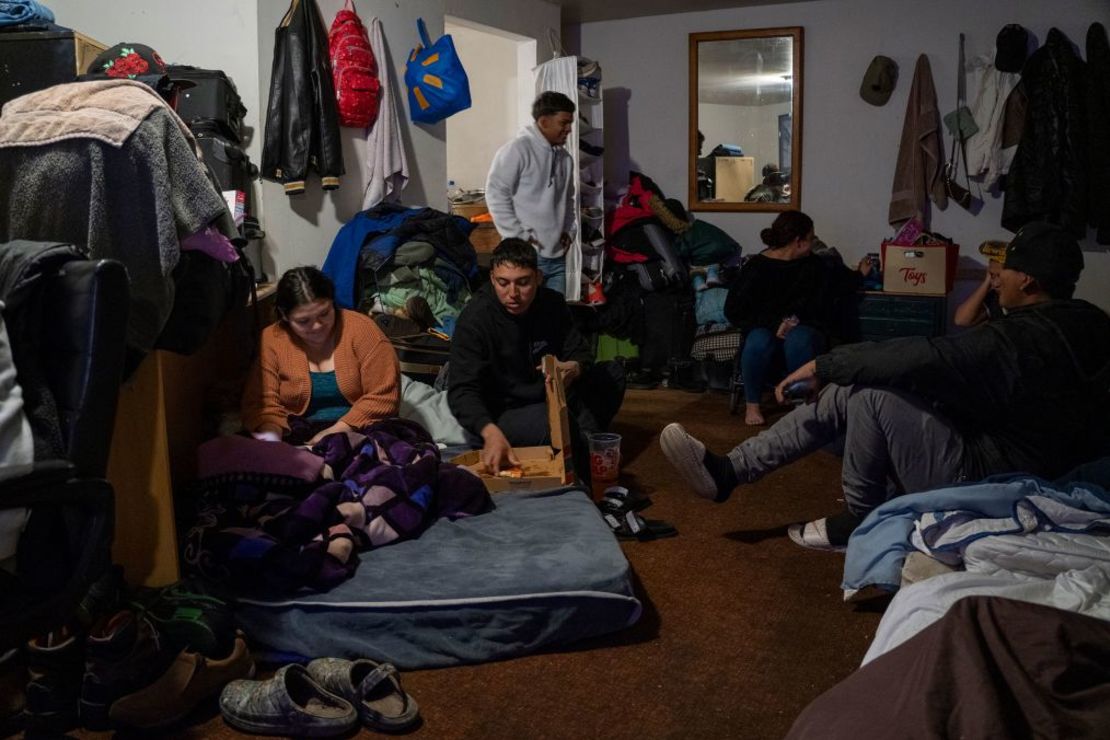 Un grupo de personas acampa en una de las habitaciones del motel de Yong Prince. Carlo, en el centro, comiendo pizza, dijo que Prince había sido como una madre para los migrantes, cocinándoles el desayuno todos los días antes de que salieran a buscar trabajo. Crédito: Evelio Contreras/CNN