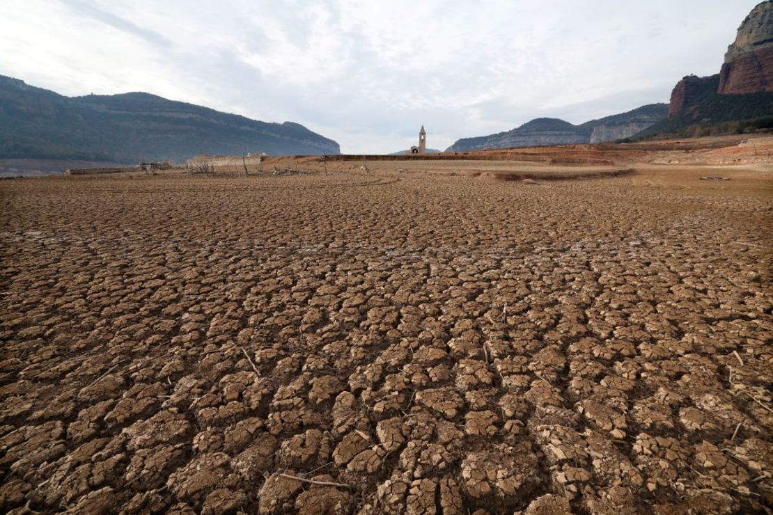 Esta fotografía tomada el 15 de enero de 2024 muestra el suelo seco junto al embalse de bajo nivel de Sau con al fondo la iglesia de Sant Roma de Sau, en la provincia de Girona, Cataluña. Crédito: LLUIS GENE/AFP vía Getty Images