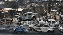 TOPSHOT - A woman with her baby walks past burned vehicles after a forest fire in Quilpue, Viña del Mar, Chile, on February 4, 2024. Chileans Sunday feared a rise in the death toll from wildfires blazing across the South American country that have already killed at least 51 people, leaving bodies in the street and homes gutted. (Photo by RODRIGO ARANGUA / AFP)