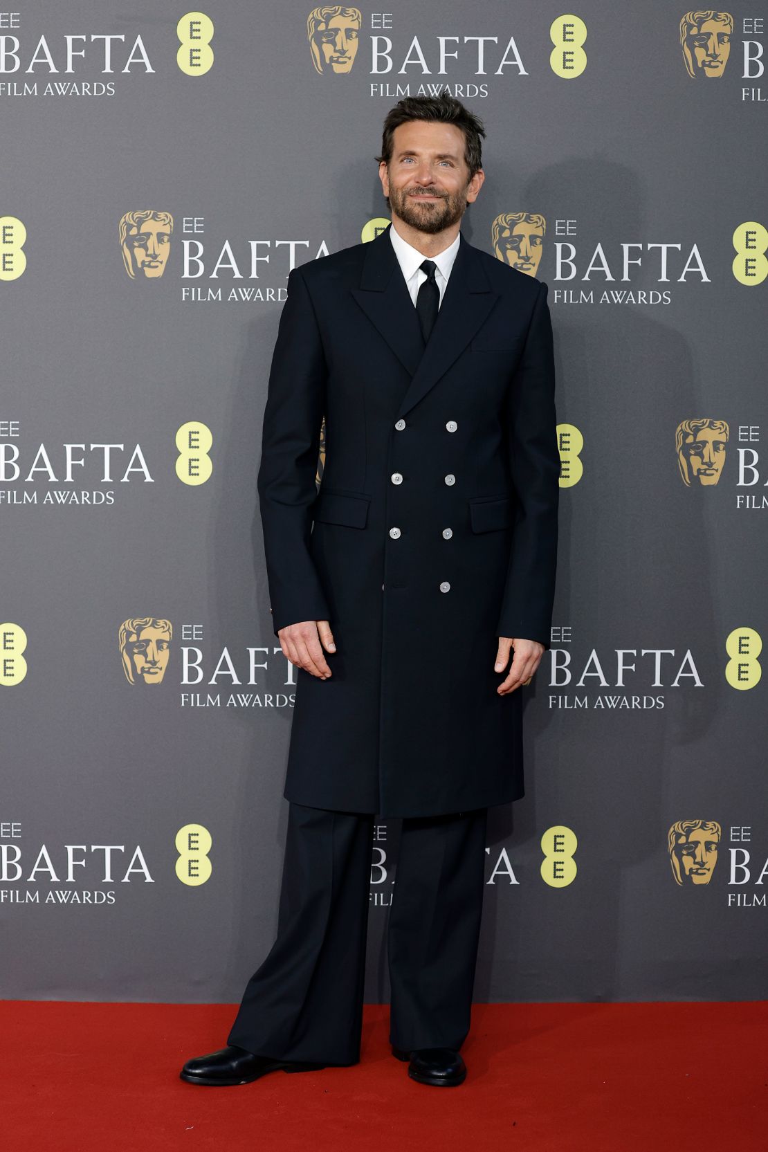 Bradley Cooper con una chaqueta cruzada larga inspirada en los años 70 y pantalones de campana de Louis Vuitton.