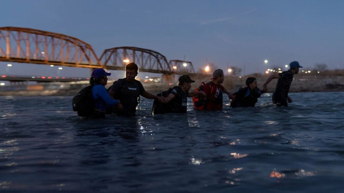 Migrantes enlazan sus brazos mientras vadean el río Grande con la intención de cruzar a Eagle Pass, Texas, el 24 de febrero de 2024.