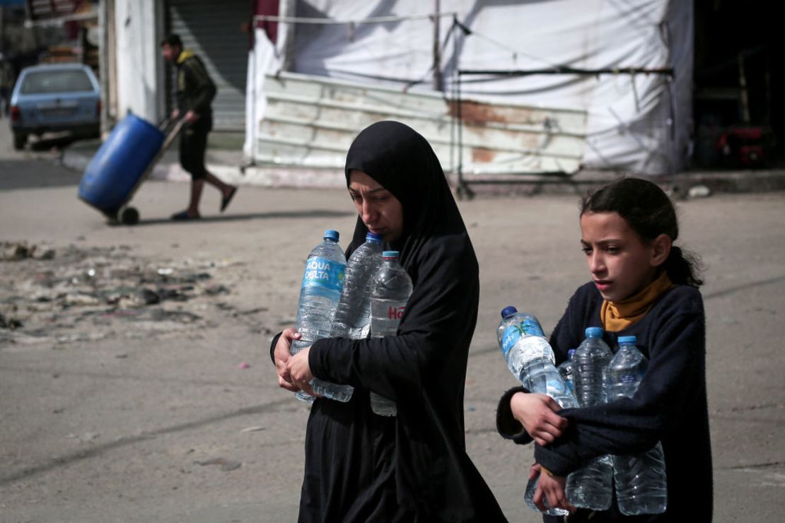 TOPSHOT - Palestinian women carry water bottles in Rafah in the southern Gaza Strip on March 1, 2024, amid ongoing battles between Israel and the Palestinian Hamas movement. (Photo by AFP)